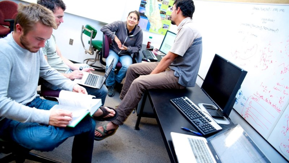 Four engineering students studying in a book and on computers. 