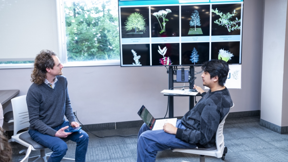 Two male students sitting in front of a screen with a digital herbarium slide on it. 