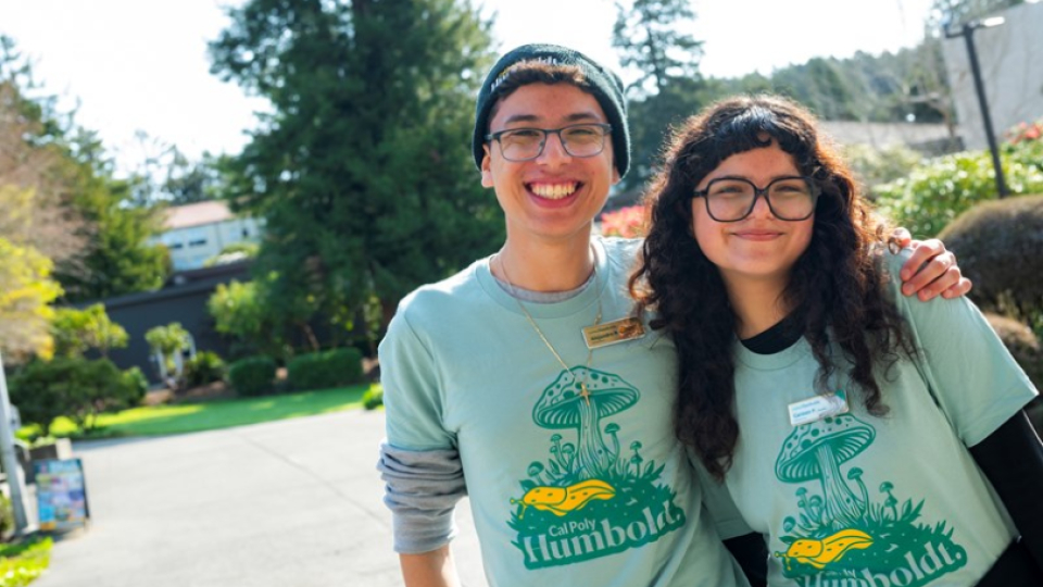Two students in glasses and matching Humboldt shirts smiling and hugging.
