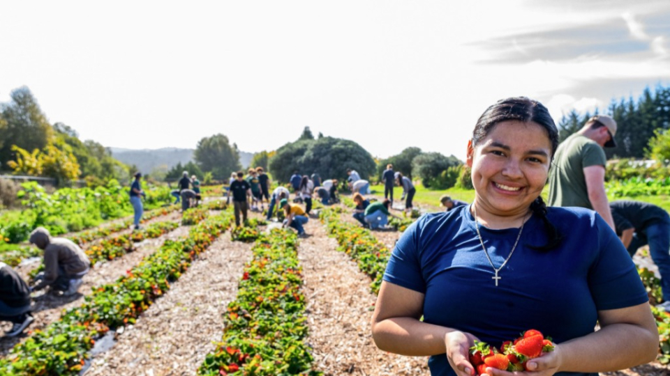 A female student smiling while holding produce and standing in a farm area.