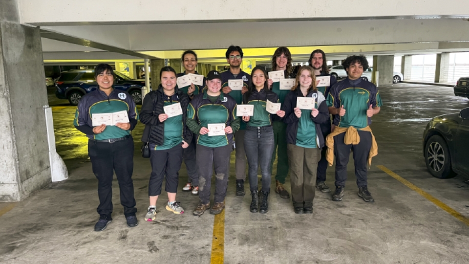 A group of archery students standing in a parking garage holding certificates. 