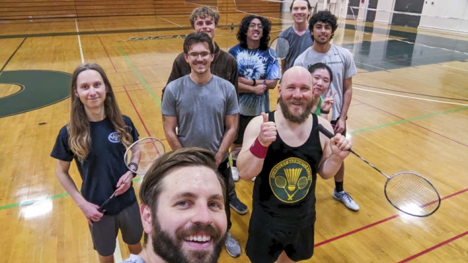 A selfie of nine badminton club members on the court with their rackets.