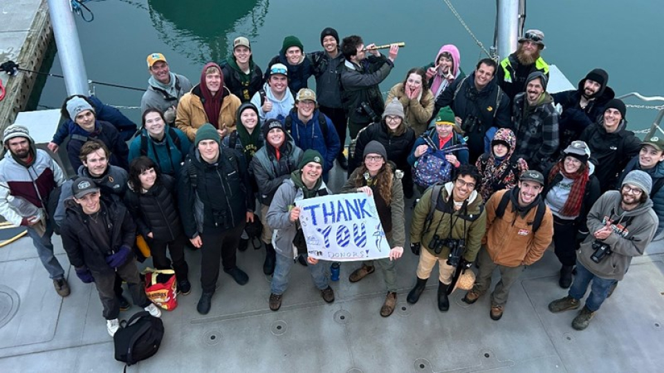 A large group of birding club members looking up at the camera holding a THANK YOU sign.