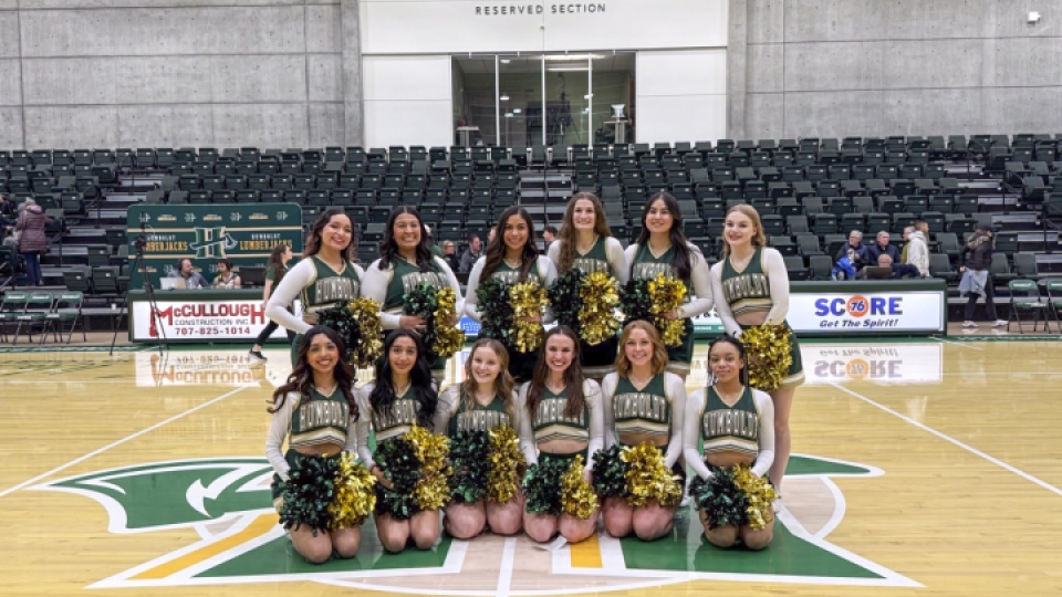 Cheer team photo in their uniforms and pom poms at center court.