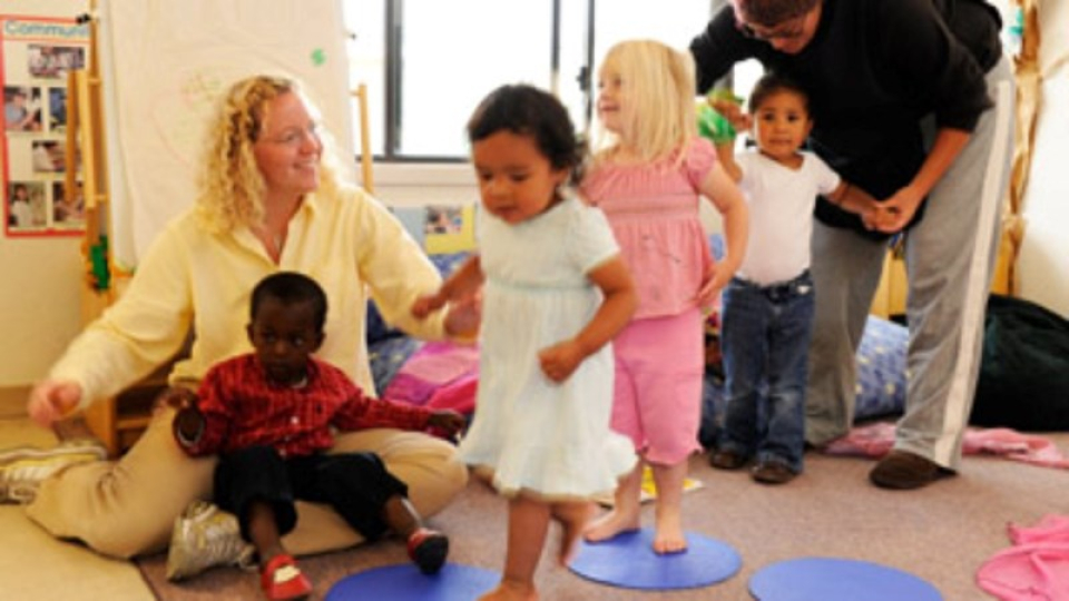 A woman on the floor with a child in her lap and smiling at three more children in line. 