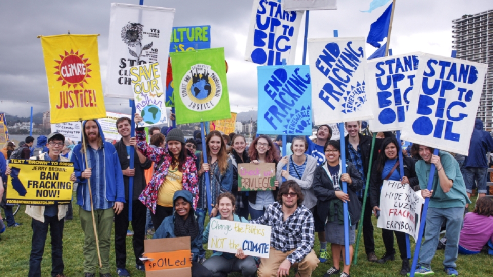 A large group of students with climate protest signs in the air at a rally.