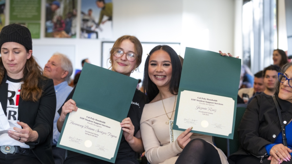 Two EOP students smiling and holding up recognition certificates in a crowd.