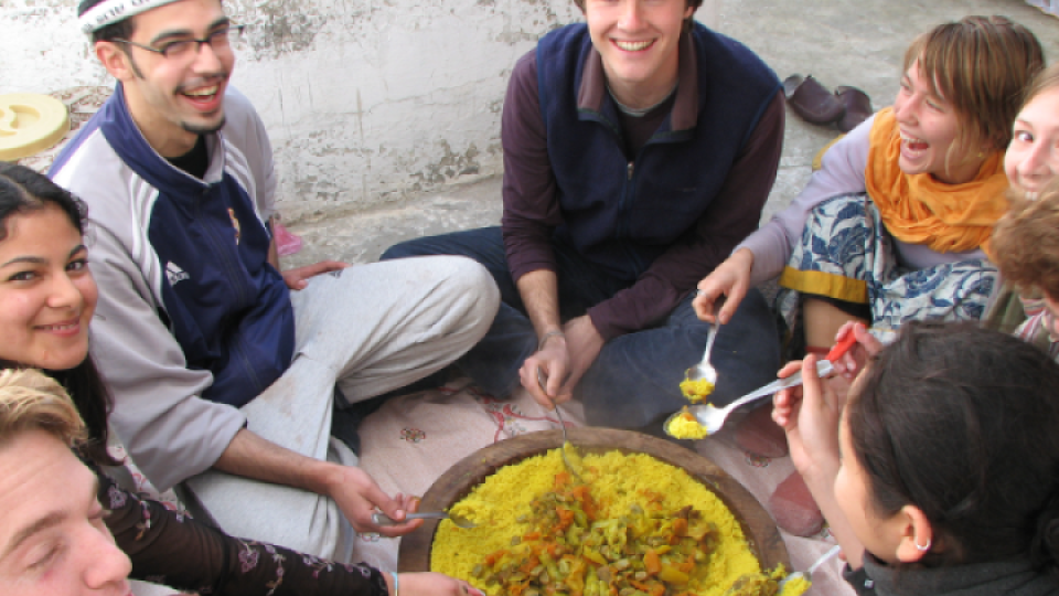 Students sitting on the ground around a pot of food.