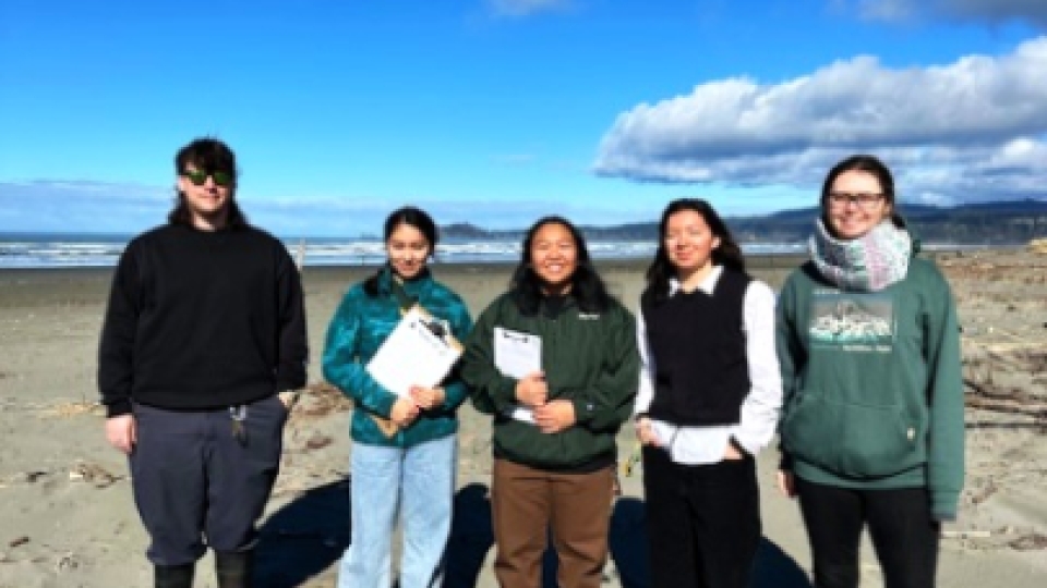 Five students standing and smiling at the beach.