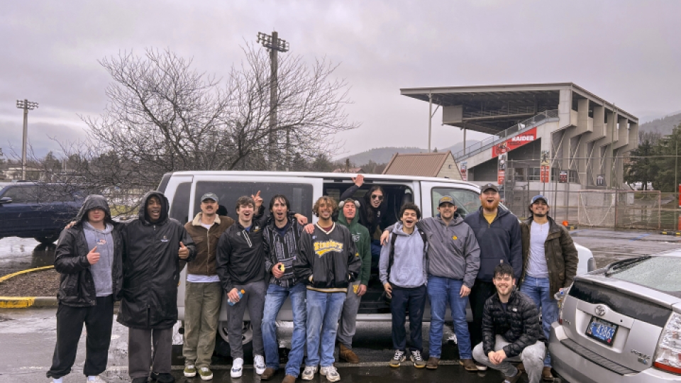 Group photo of men's lacrosse players in the rain outside of a van.