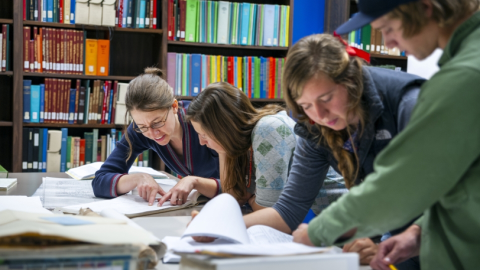 Four students reviewing manuscripts at a table in the library.