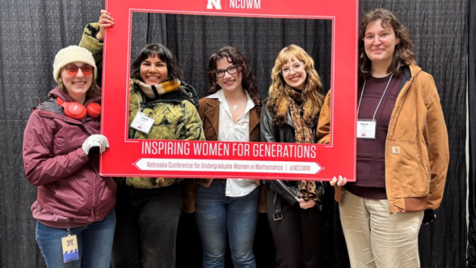 Five women math majors standing with a giant red frame at a math conference.