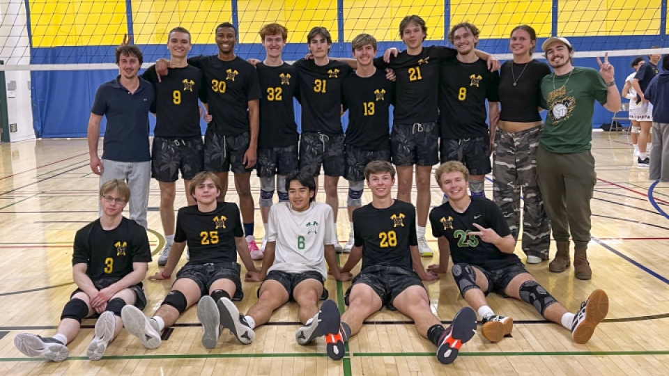 The men's volleyball team posing on the court with a net behind them.