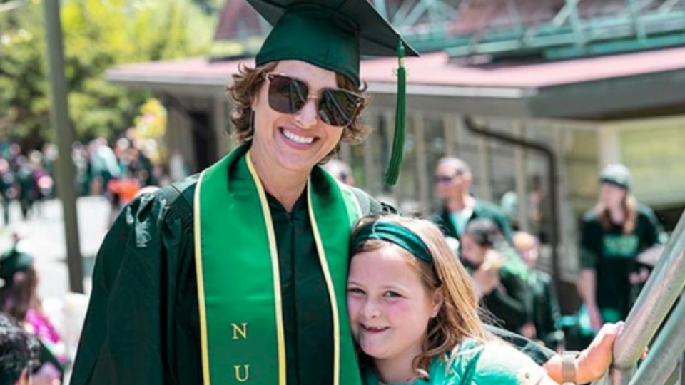 A nursing grad smiling in graduation regalia hugging her child.