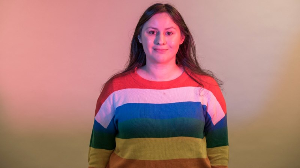 A student with long hair in a rainbow stripe sweater. 
