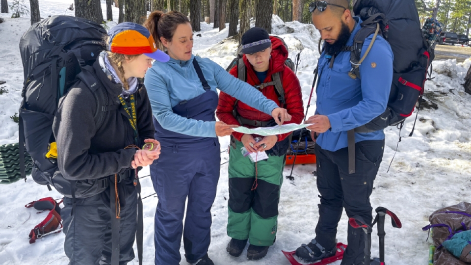 Four recreation students and faculty reviewing a map outside in the snow.