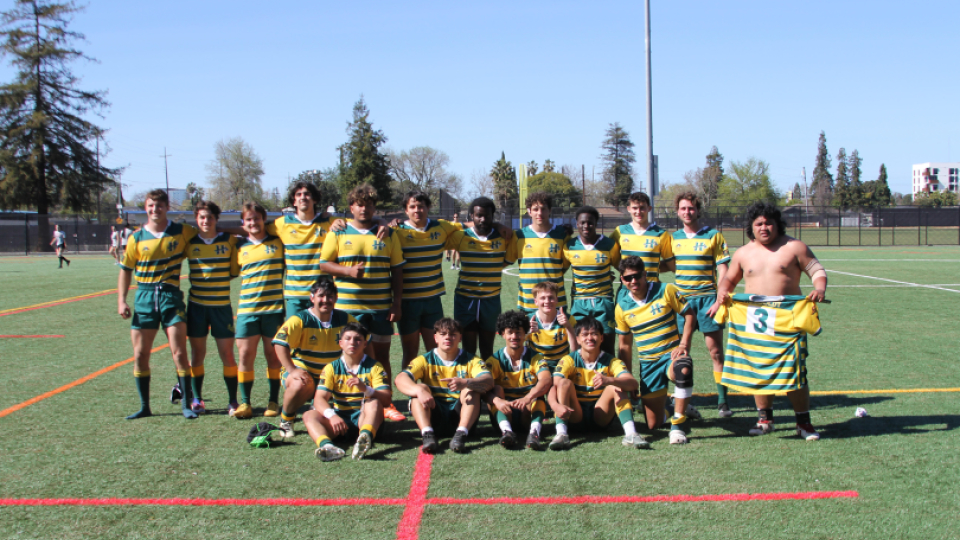 Team photo of the men's rugby club in yellow jerseys on the field.