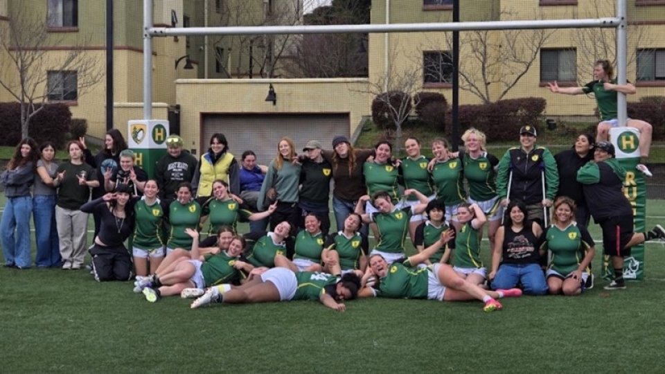 Humboldt women's rugby team in uniform posing in front of the goal posts on the field.