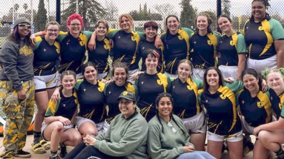 Team photo of women's rugby team in uniform in front of a field.