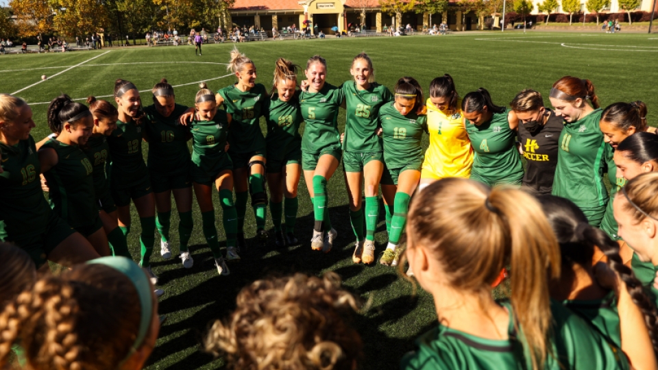 The women's soccer team celebrating in a circle after a game. 