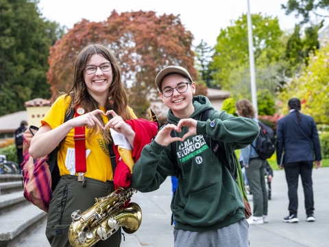 A photo of two students holding up their hands as hearts on campus.