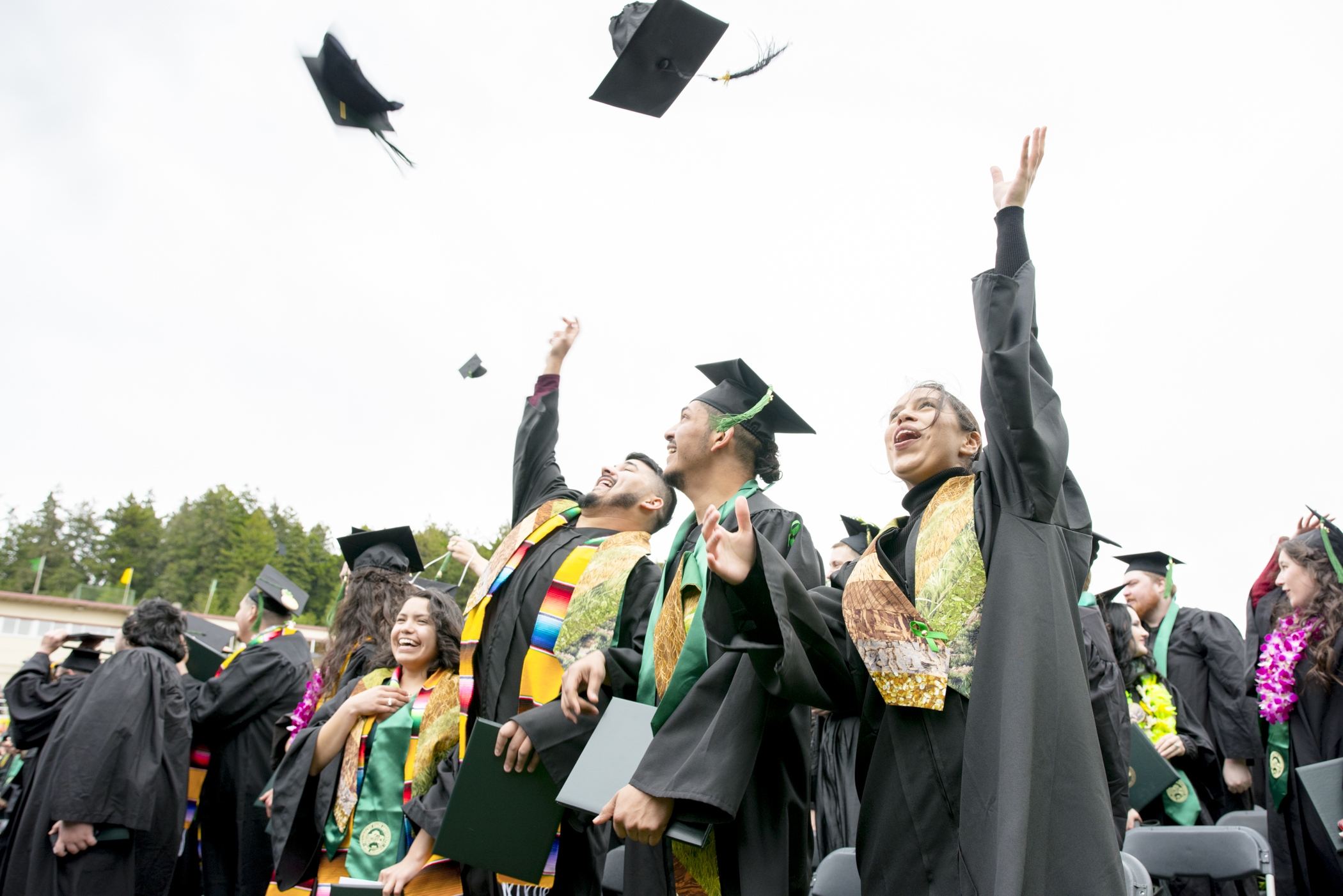 Cal Poly Humboldt students at graduation throwing their caps in the air
